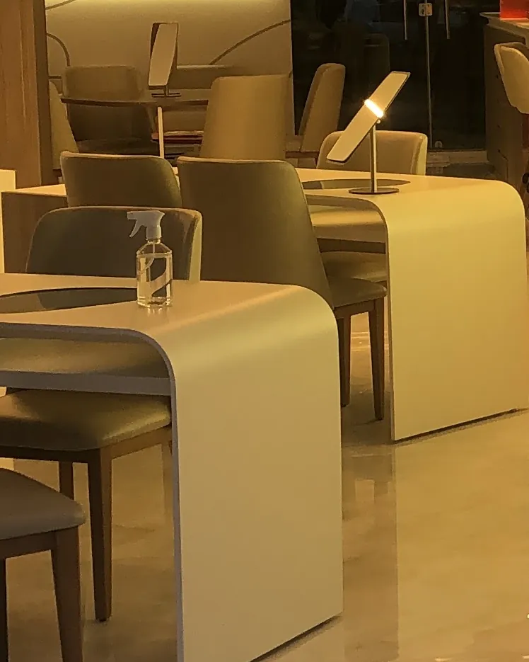 Mesas de atendimento brancas com cadeiras bege e um espelho de mesa, dentro da loja